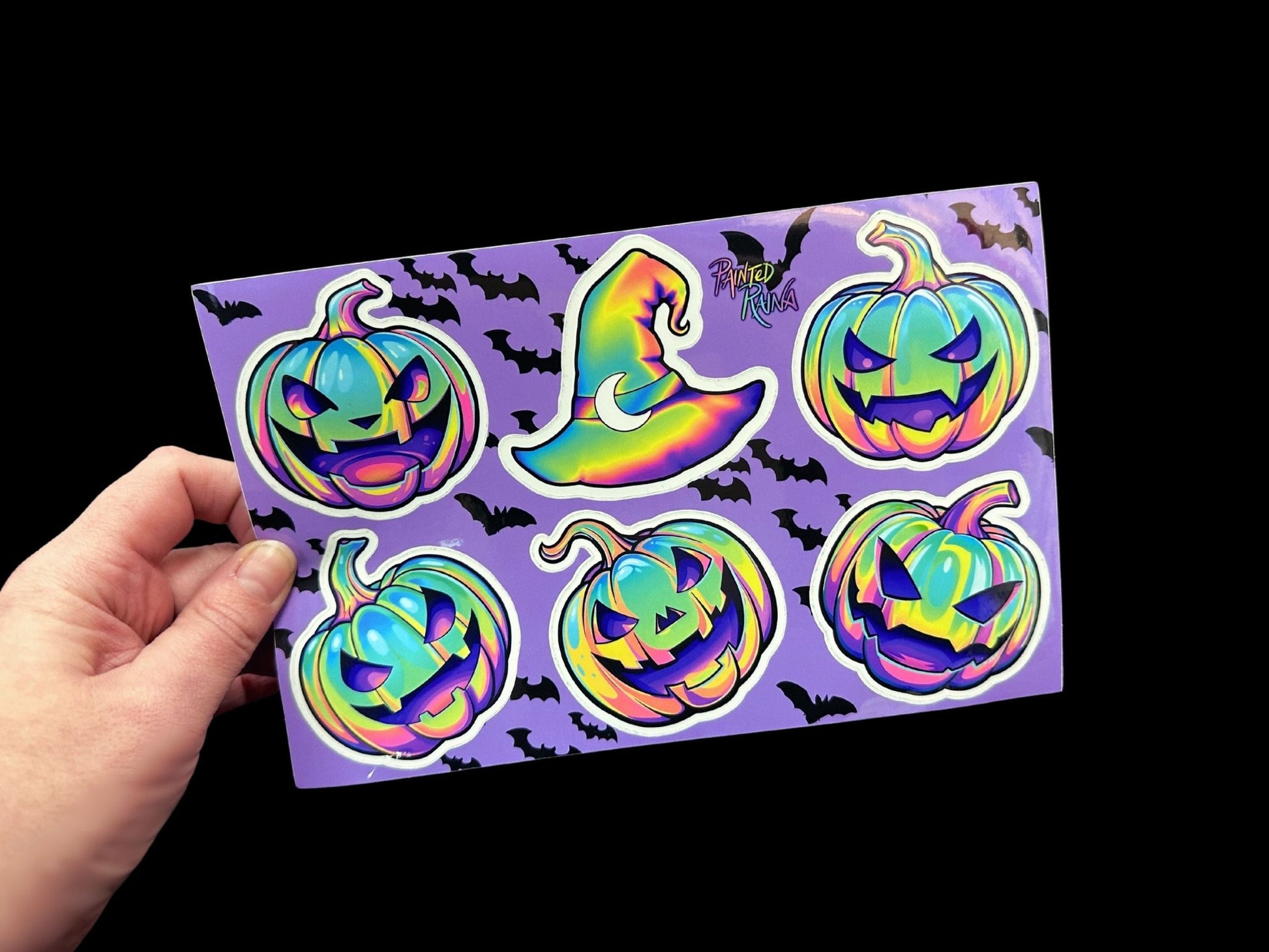 a hand holding a purple sticker with halloween pumpkins on it